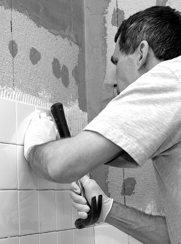 Man setting tile on cement board. He is tapping the tile in place with the handle of a hammer. Closeup. Real person on the job.